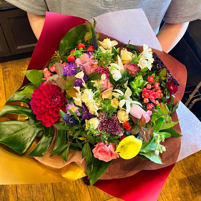 Sissi Flower Design JPのボリューム感あるおまかせブーケL。赤やピンク、黄色の花々と大きなモンステラの葉が華やかにラッピングされています。